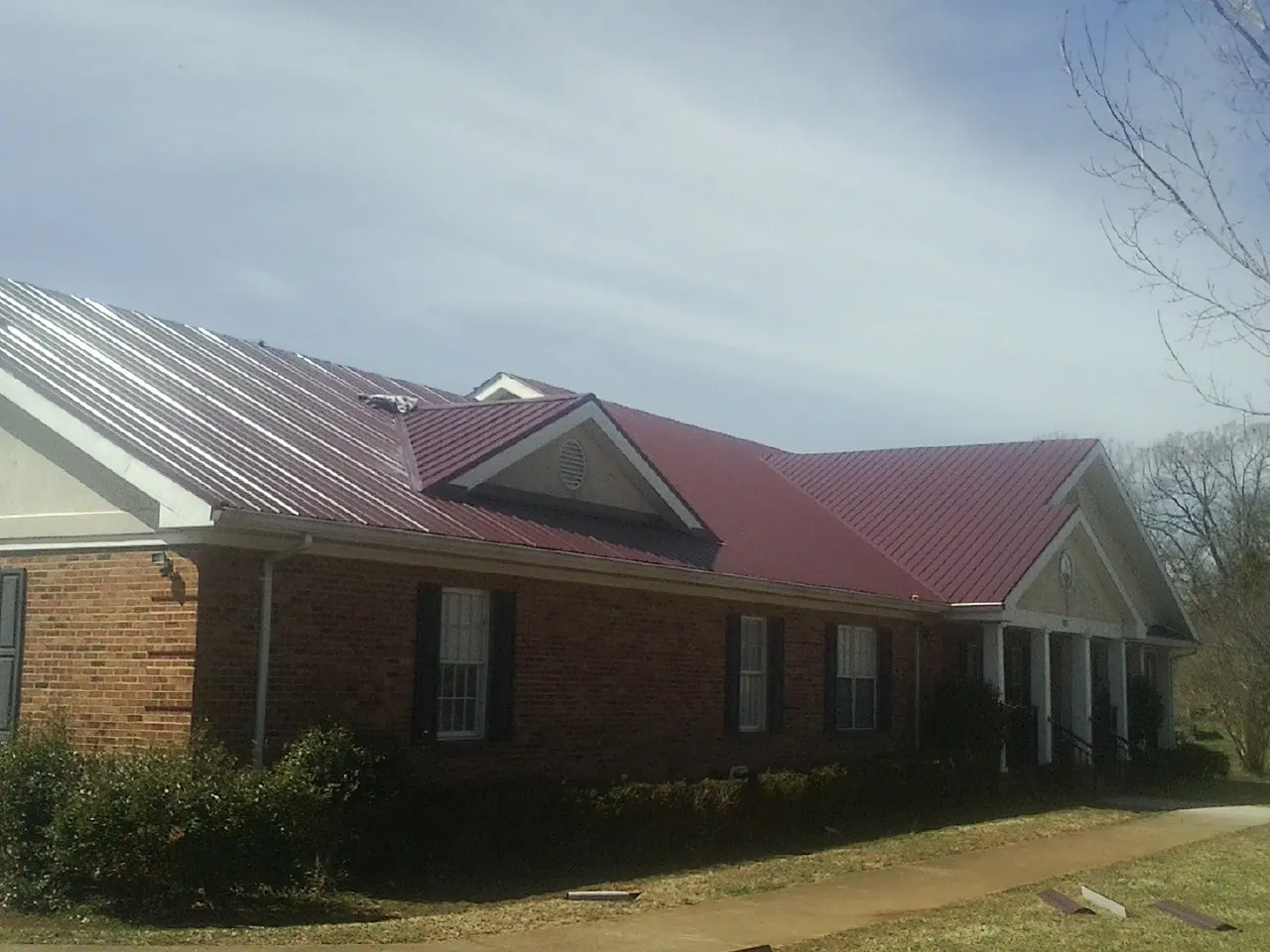 Red metal roof with gabled entries on a long brick building, from a Hail Damage Roof Repair job in Nanty Glo