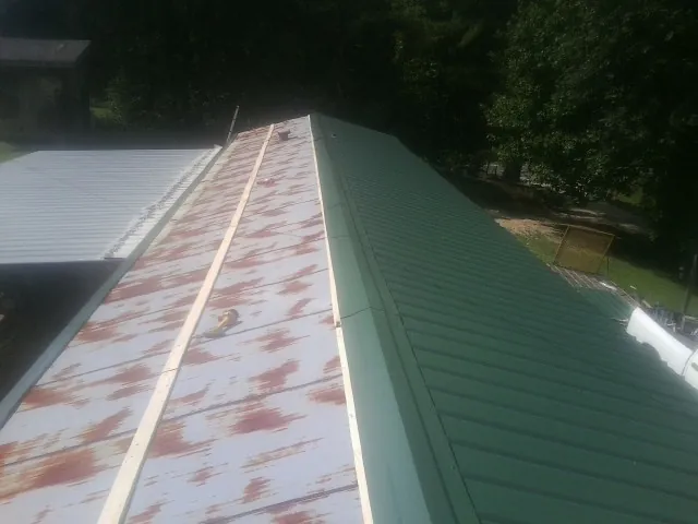 Old rusted panels beside newly installed green metal roofing — Wind Damage Roof Repair by Roofing Brothers in Nanty Glo
