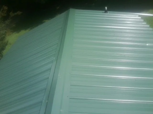 New green metal panels meeting at the ridge of a roof — Flat Roof Repair work by our crew in Nanty Glo