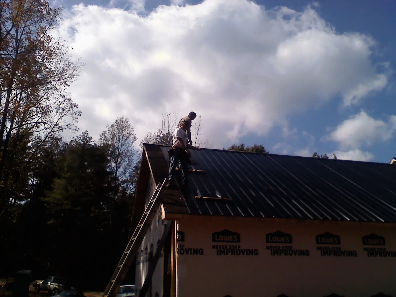 Roofer fastening dark metal panels high against a cloudy sky, from a Roof Inspection job in Nanty Glo