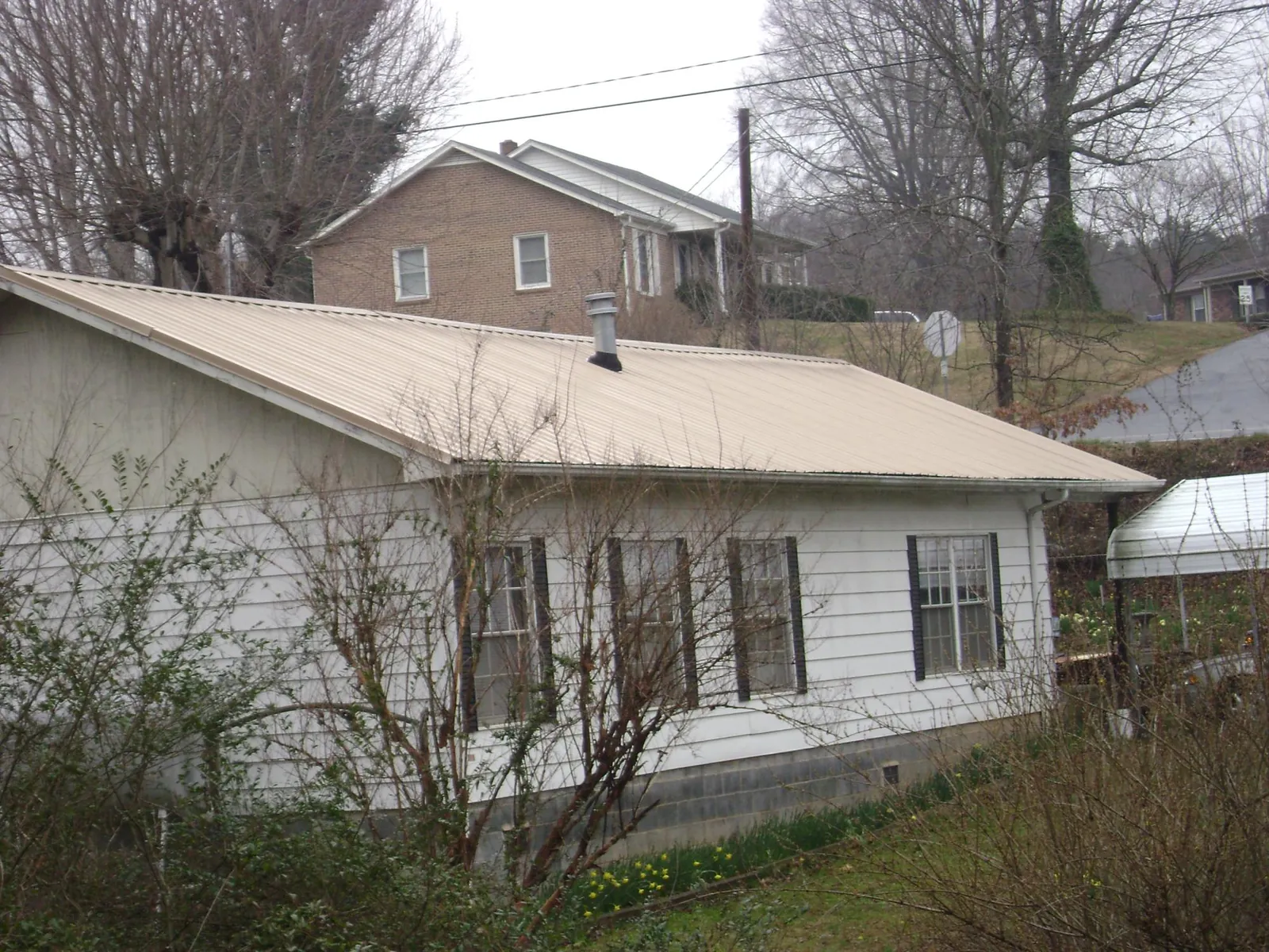 Tan metal roof on a white sided house set into a hillside — Commercial Roofing by Roofing Brothers in Nanty Glo