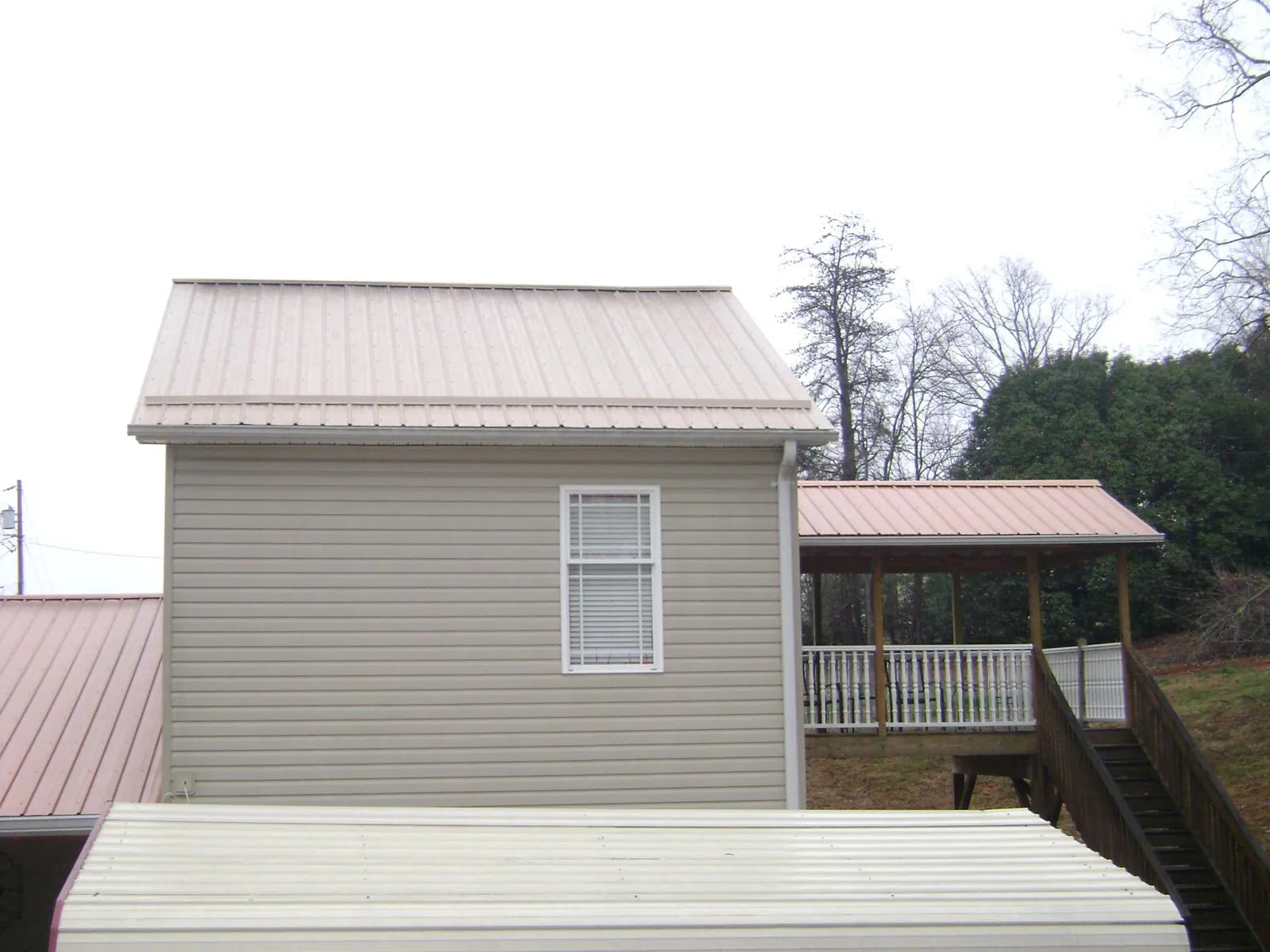 Tan metal roofs on a two story addition and attached porch, from a Roof Replacement job in Nanty Glo